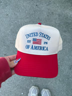 A red and off-white snapback cap, featuring 'UNITED STATES OF AMERICA' est. 1776 and an American flag graphic on the front.
