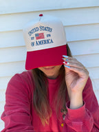A person wearing a red and white trucker-style baseball cap with 'UNITED STATES OF AMERICA EST 1776' embroidered on the front, posed in front of white siding.